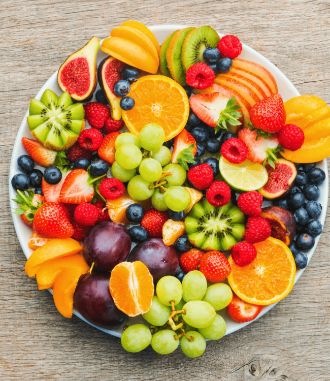 Plato redondo con frutas variadas cortadas y enteras organizadas de forma decorativa